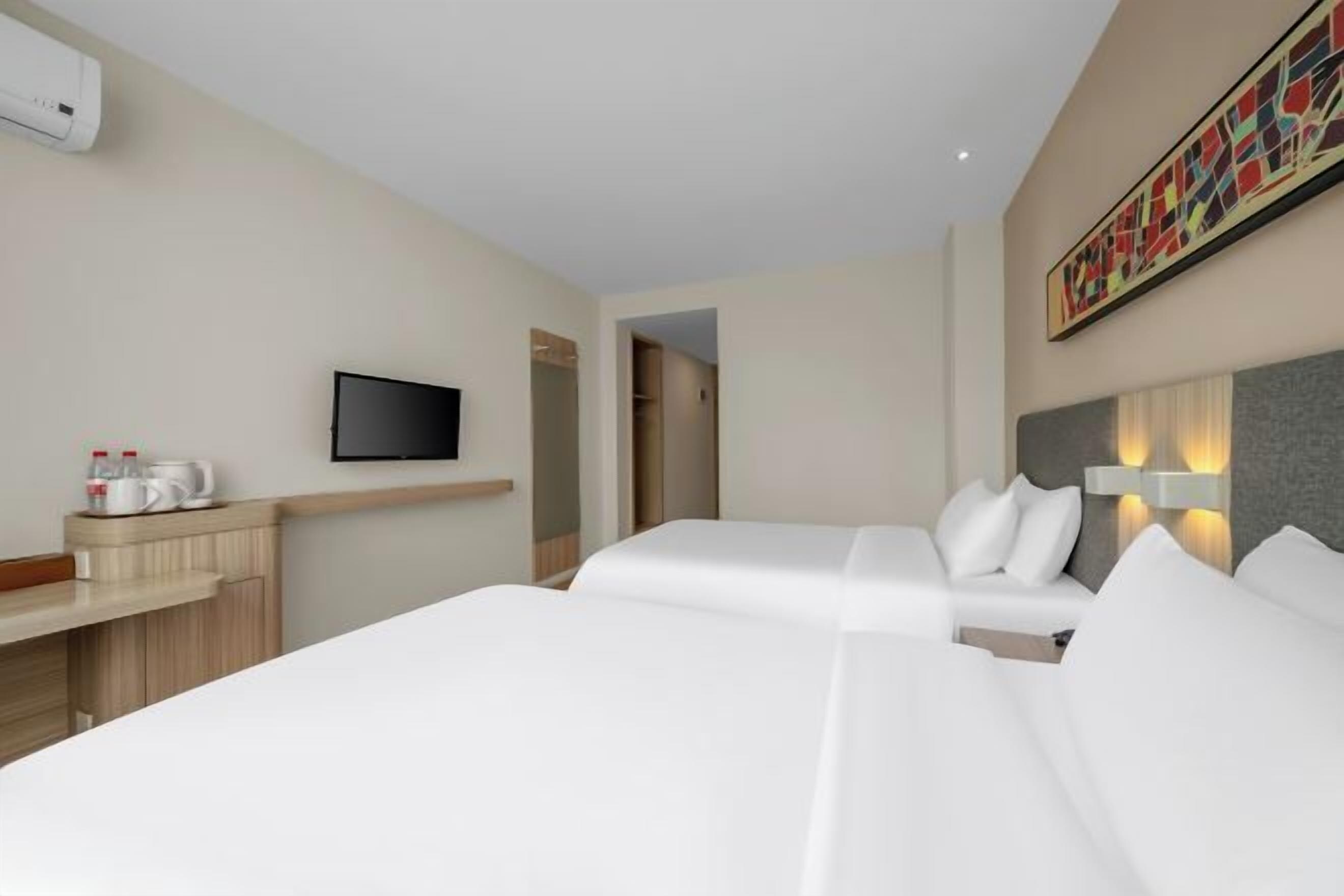 Habitación de hotel con dos camas, un televisor, un escritorio con cafetera y un cuadro en la pared.
