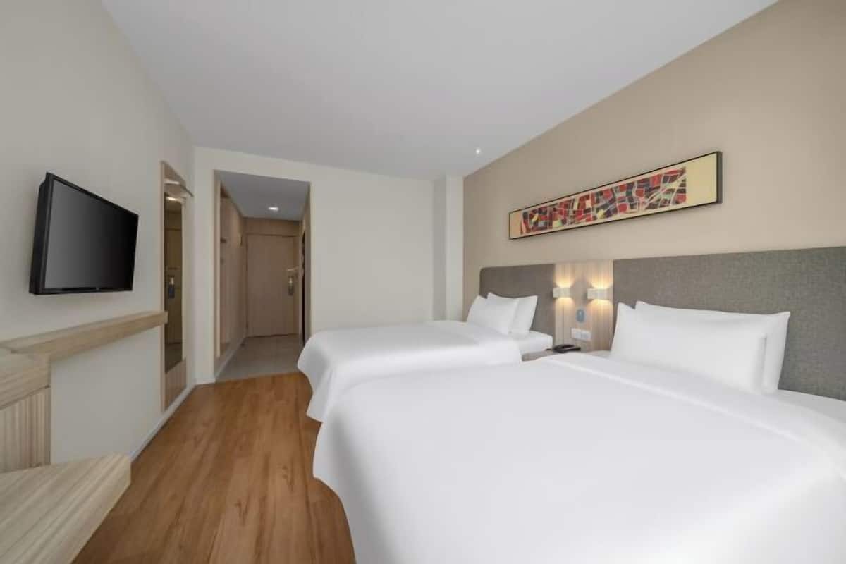 A hotel room with two beds, a television, and a hallway leading to another room.