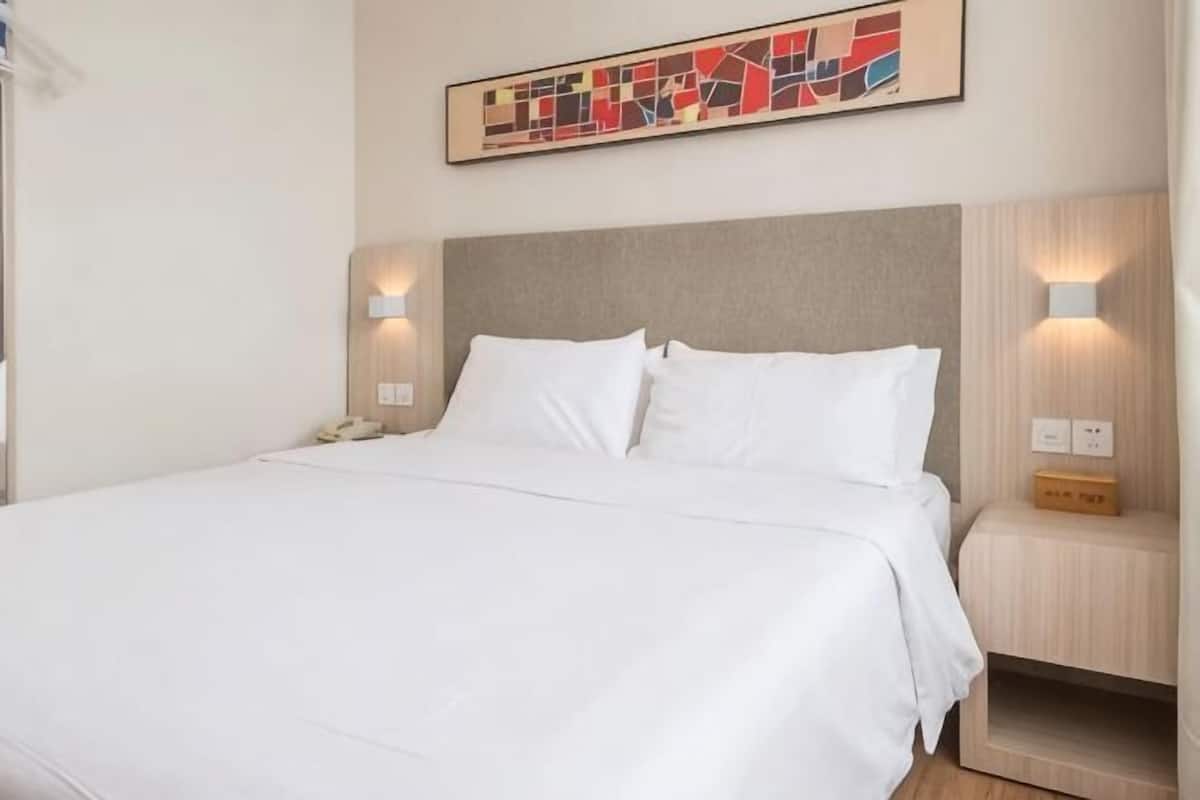 A neatly made bed with white linens, a headboard with a light-colored panel, and two bedside lamps on either side.