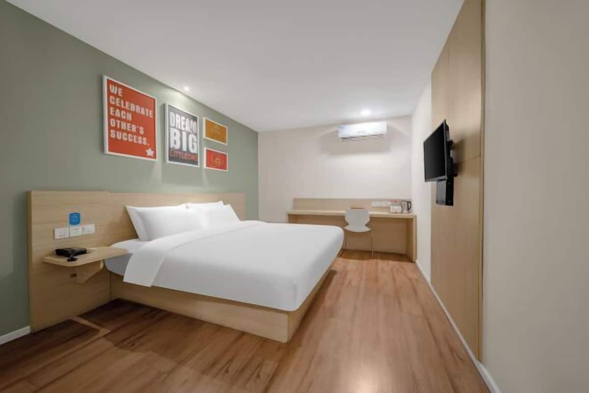 A hotel room with a bed, bedside table, desk, chair, and a TV mounted on the wall.