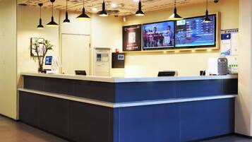 A reception desk with a flat-screen TV, a plant, and a digital display.