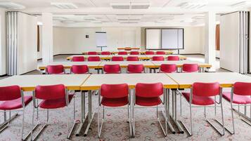 A conference room with rows of tables and chairs, white walls, and a projector screen.