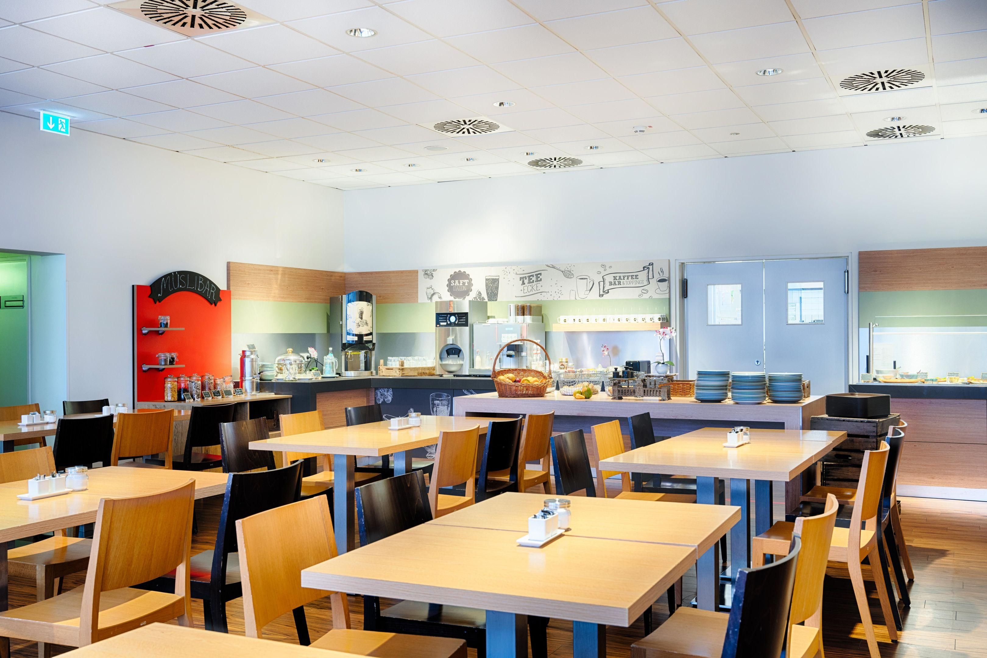 A modern cafe with wooden tables and chairs, a counter with a coffee machine, and a menu board.