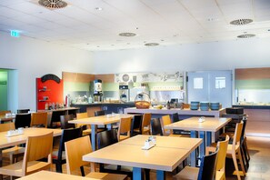 Un café moderne avec des tables et des chaises en bois, un comptoir avec une machine à café et un tableau affichant le menu.