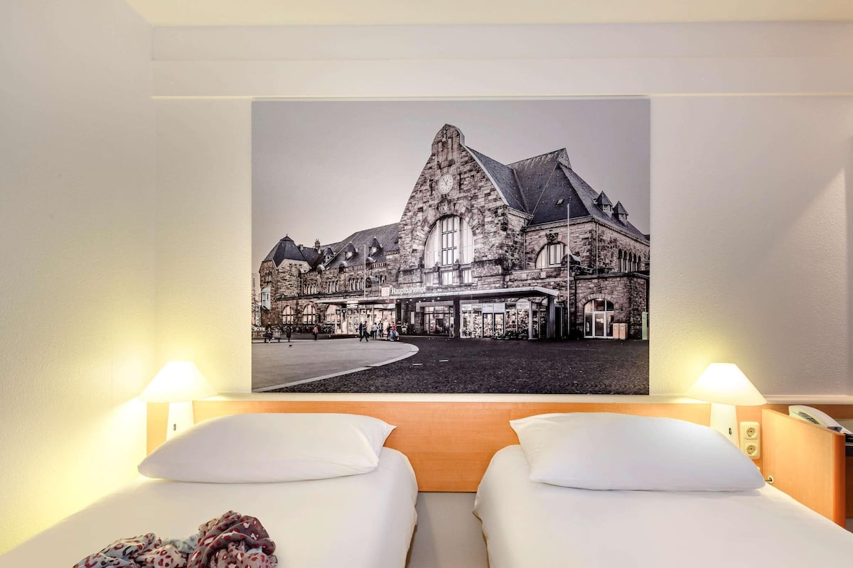 A hotel room with two beds, a large framed picture of a historic building, and two bedside lamps.