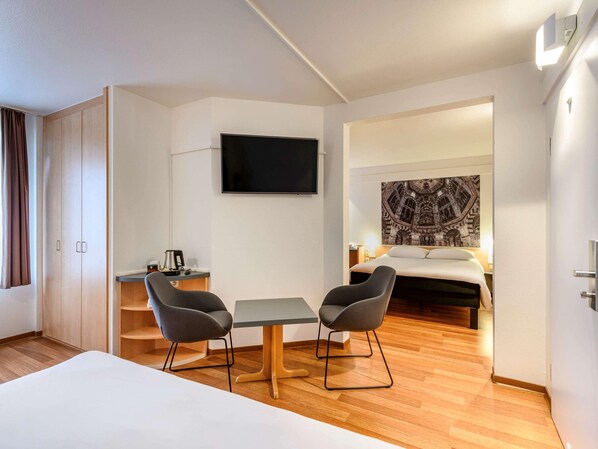A hotel room with a bed, two chairs, a table, a TV, and a painting on the wall. - B&B Aachen HBF (Aachen)