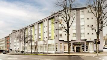 Ein modernes Hotel mit einem zentralen Eingang, großen Fenstern und einem vertikalen, grünen Streifen.