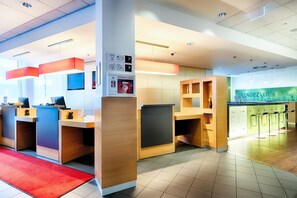 En moderne hotellobby med træreceptionister, et rødt tæppe og et barområde med barstole.