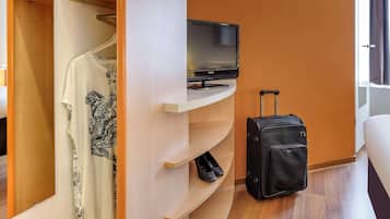 Habitación de hotel con televisor sobre un soporte, una maleta y un armario con estantes.