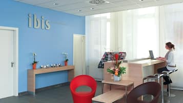 Zona de recepción con pared azul, mostrador de madera, sillas rojas y marrones, y una planta en maceta.