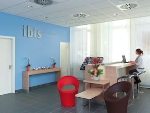 A reception area with a blue wall, a wooden reception desk, red and brown chairs, and a potted plant.