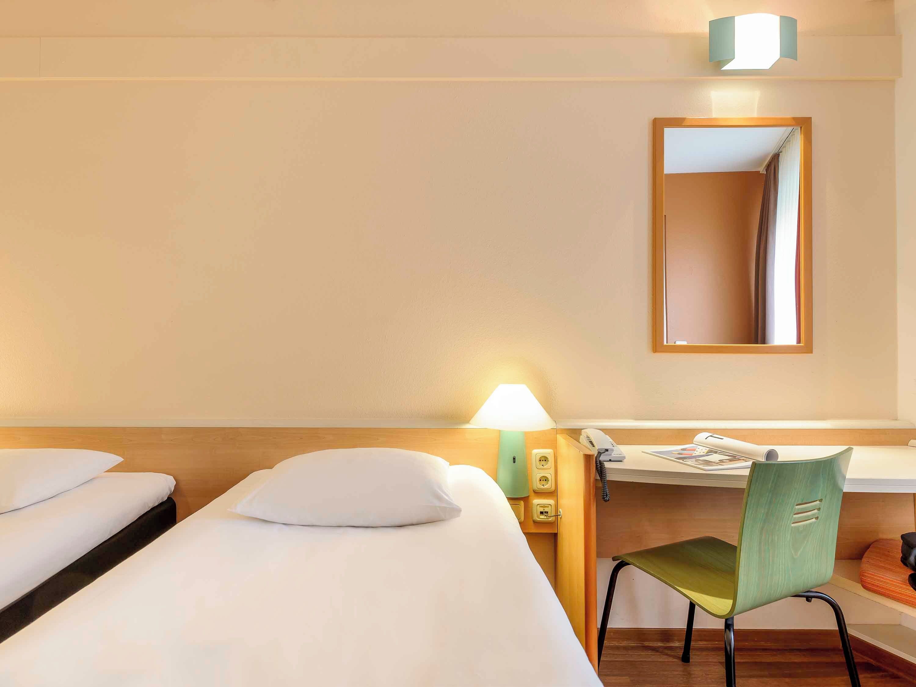 Habitación de hotel con una cama individual, un escritorio con silla, un teléfono y un espejo en la pared.