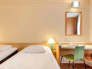 A hotel room with a single bed, a desk with a chair, a telephone, and a mirror on the wall.