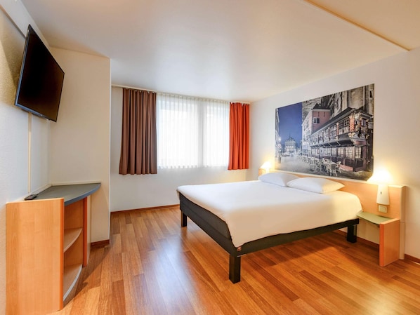 Une chambre d’hôtel avec un lit, un bureau, une télévision et un tableau au mur.