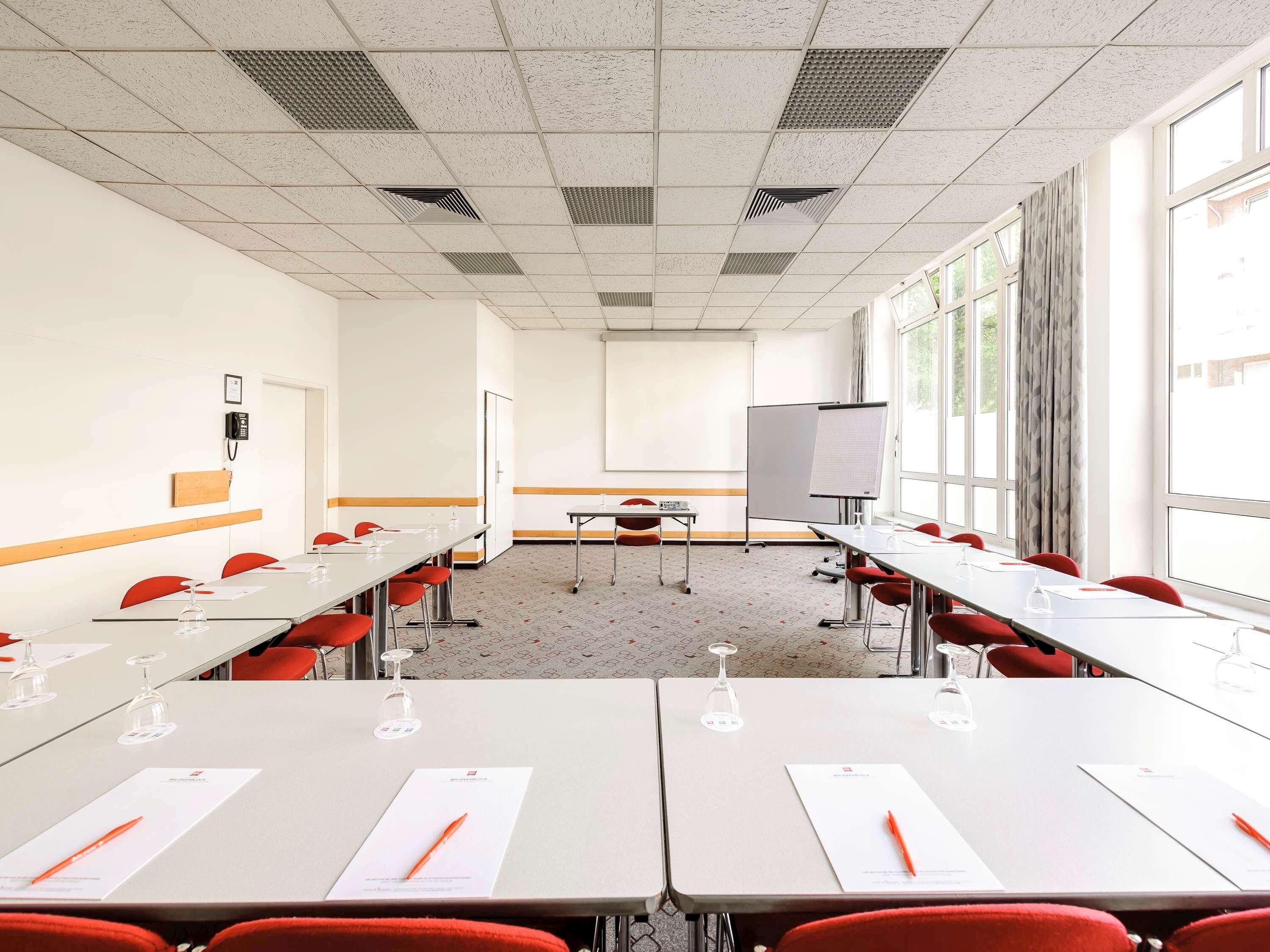 Ein Konferenzraum mit Tischen, Stühlen, einer Tafel und einer Projektionsleinwand.