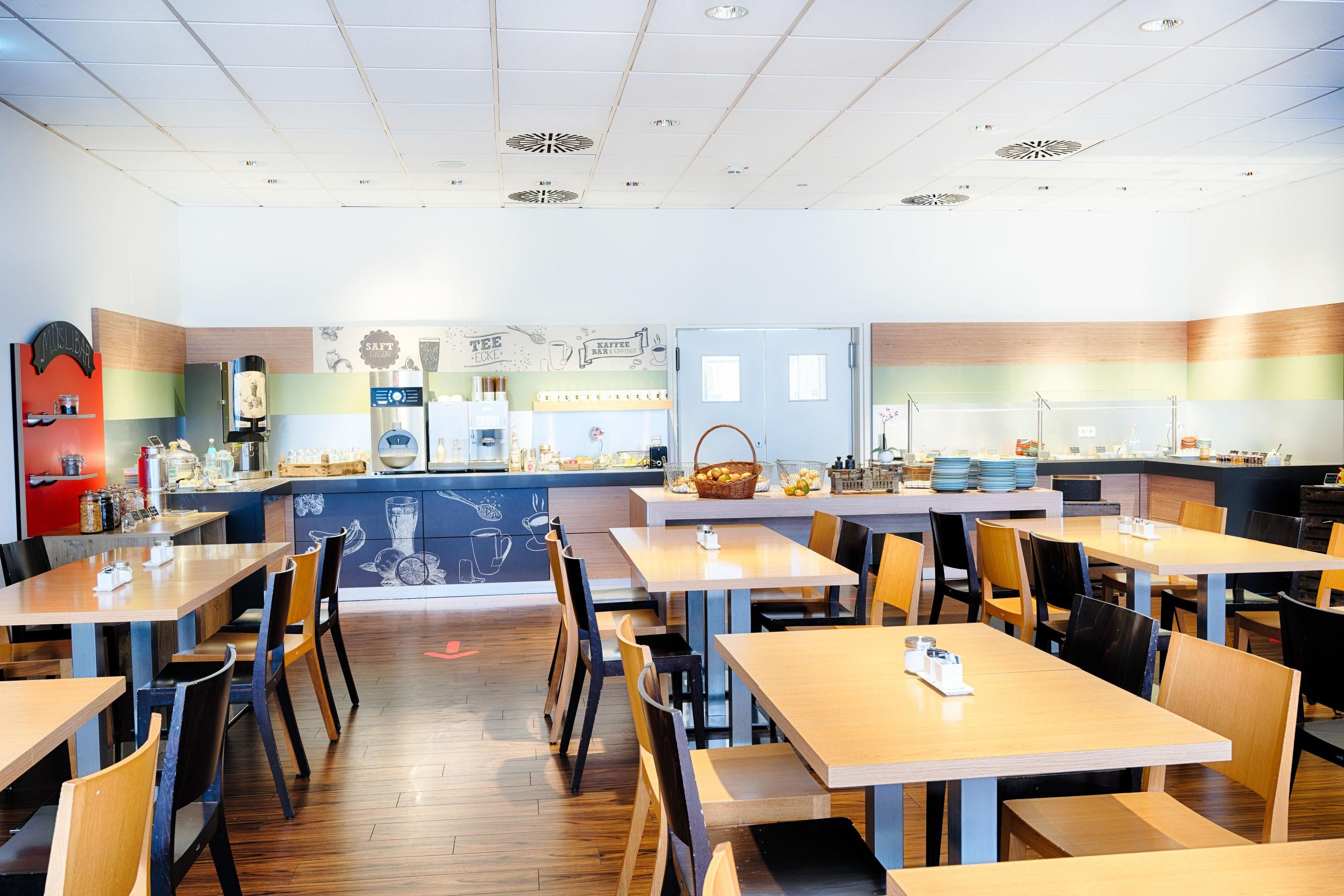 Ein Café mit Holztischen und -stühlen, einer Theke mit Kaffeemaschine und einer Wand mit einer Kaffeemural.