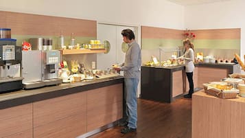 Un área de cocina moderna con estación de café, refrigerador y mesa de buffet con diversas opciones de comida.