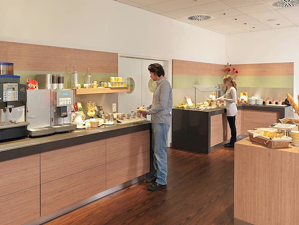 A modern kitchen area with a coffee station, a refrigerator, and a buffet counter with various food items.