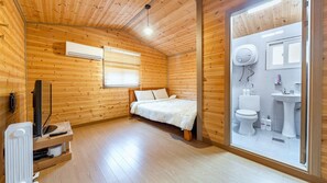 Une chambre dans un chalet en bois, comprenant un lit, une télévision et une salle de bain avec des toilettes et un lavabo.