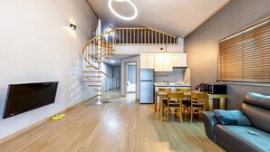 Een modern appartement met een spiltrap, een keuken, een eethoek en een woonkamer met een bank en televisie.