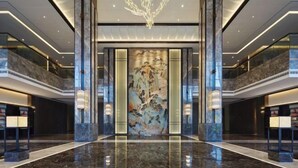 Un moderno vestíbulo de hotel con piso de mármol, un cuadro abstracto de gran tamaño y una lámpara de araña singular.