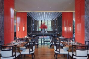A restaurant with multiple tables and chairs, a central seating area, and a large vase with red flowers. - Tianyuan Mingyue Hotel (Jingning)