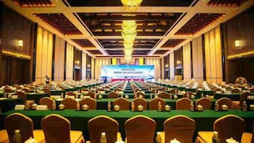 A conference room with rows of tables and chairs, a large screen at the front, and a chandelier.