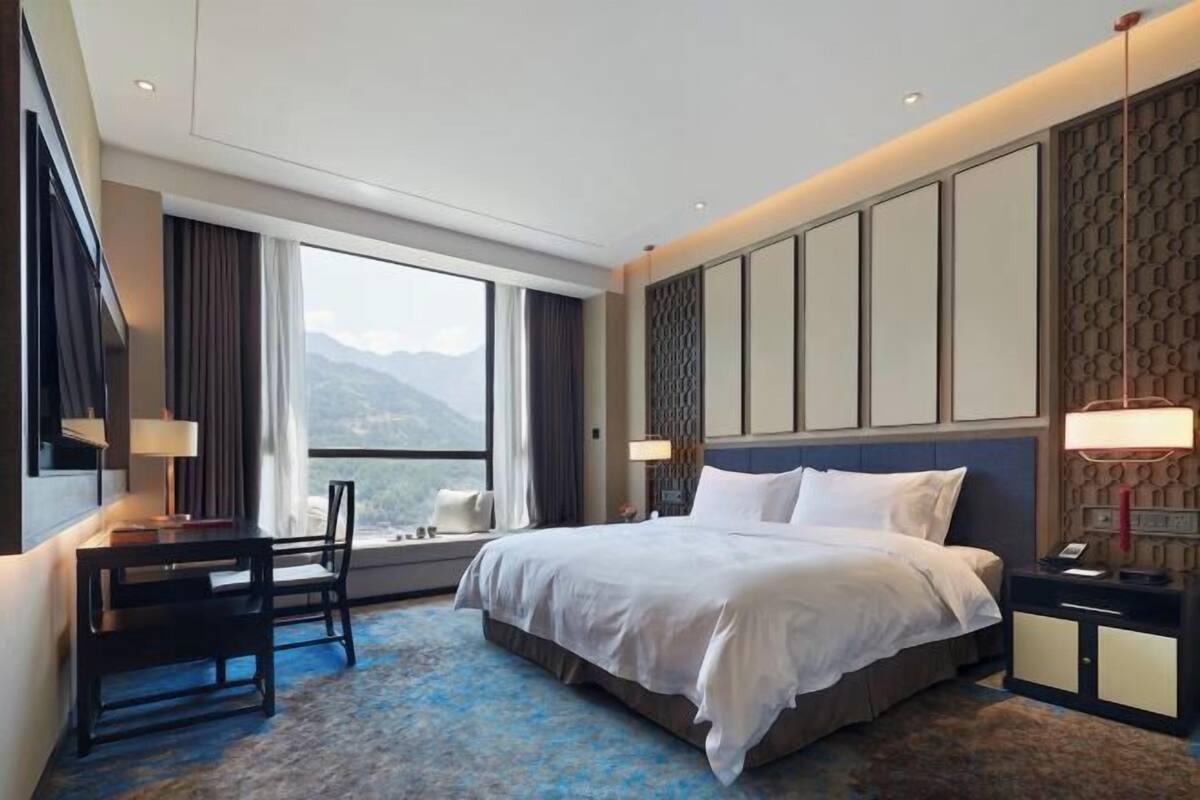 Habitación de hotel con cama, escritorio, silla y vistas a montañas.