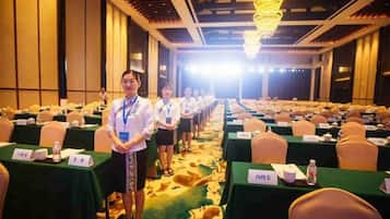 A conference room with rows of tables, nameplates, and a person standing at the front.