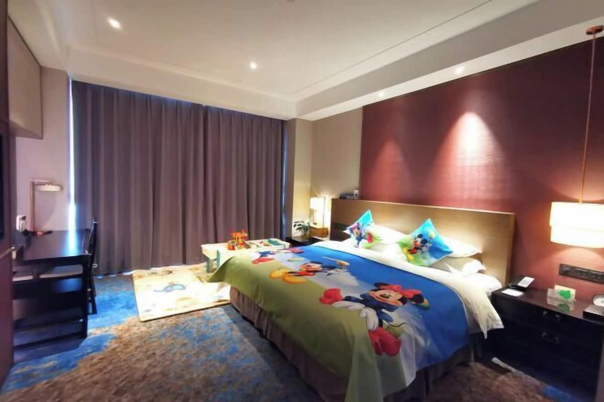 Una habitación de hotel con una cama, un escritorio, una silla, una mesita de noche y una lámpara.