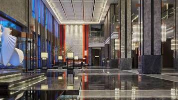 A modern hotel lobby with a marble floor, a reception desk, and a large statue.