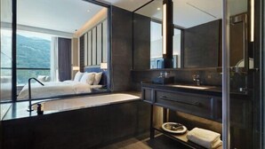 Una habitación de hotel moderna con una cama grande, una bañera empotrada, un espejo amplio y vistas a las montañas.