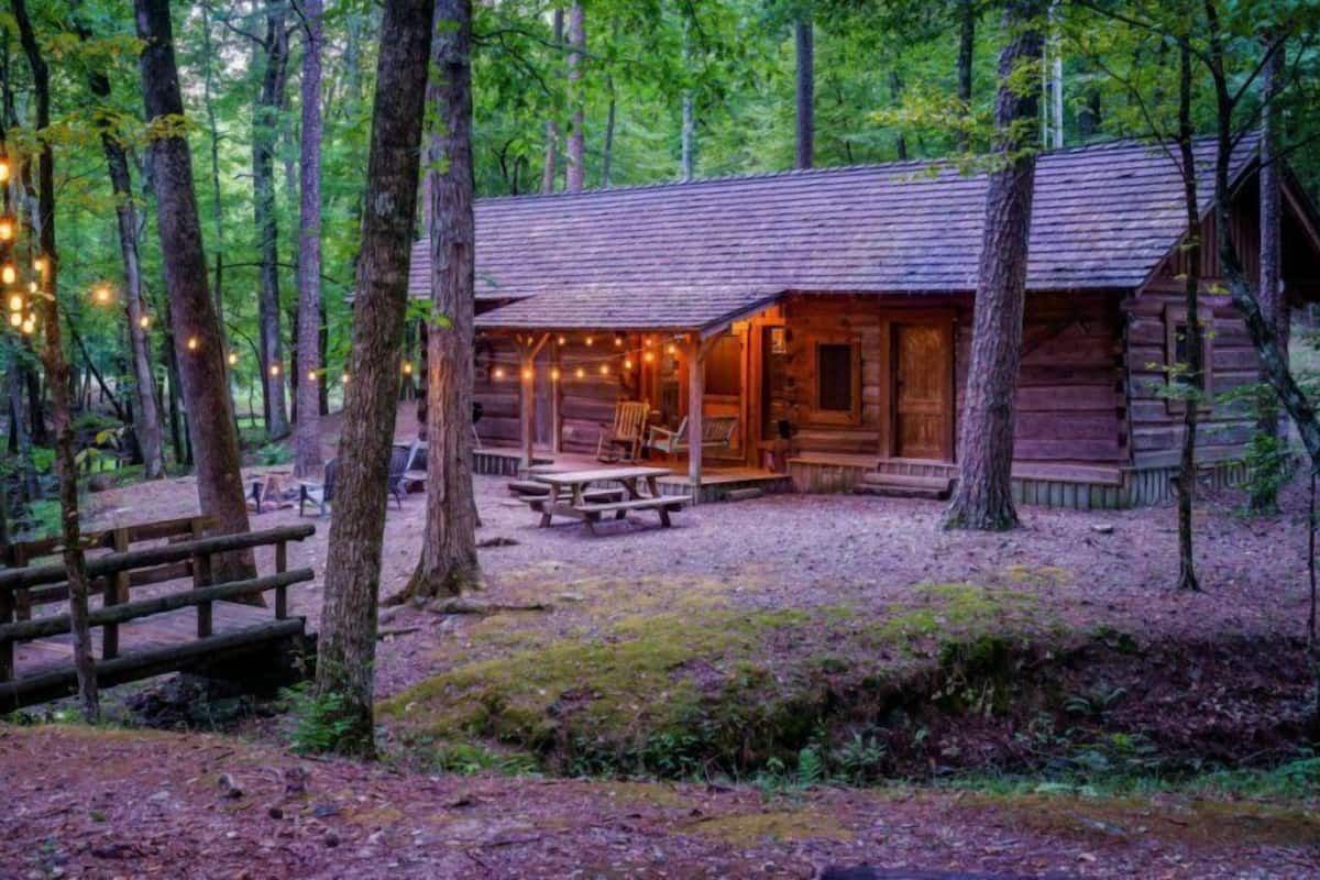 Een rustieke blokhut met een veranda, picknicktafels en lichtslingers.