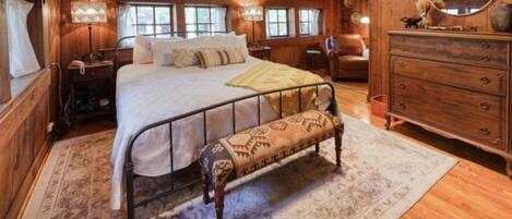 A wooden-themed bedroom with a bed, bench, dresser, and a mirror.