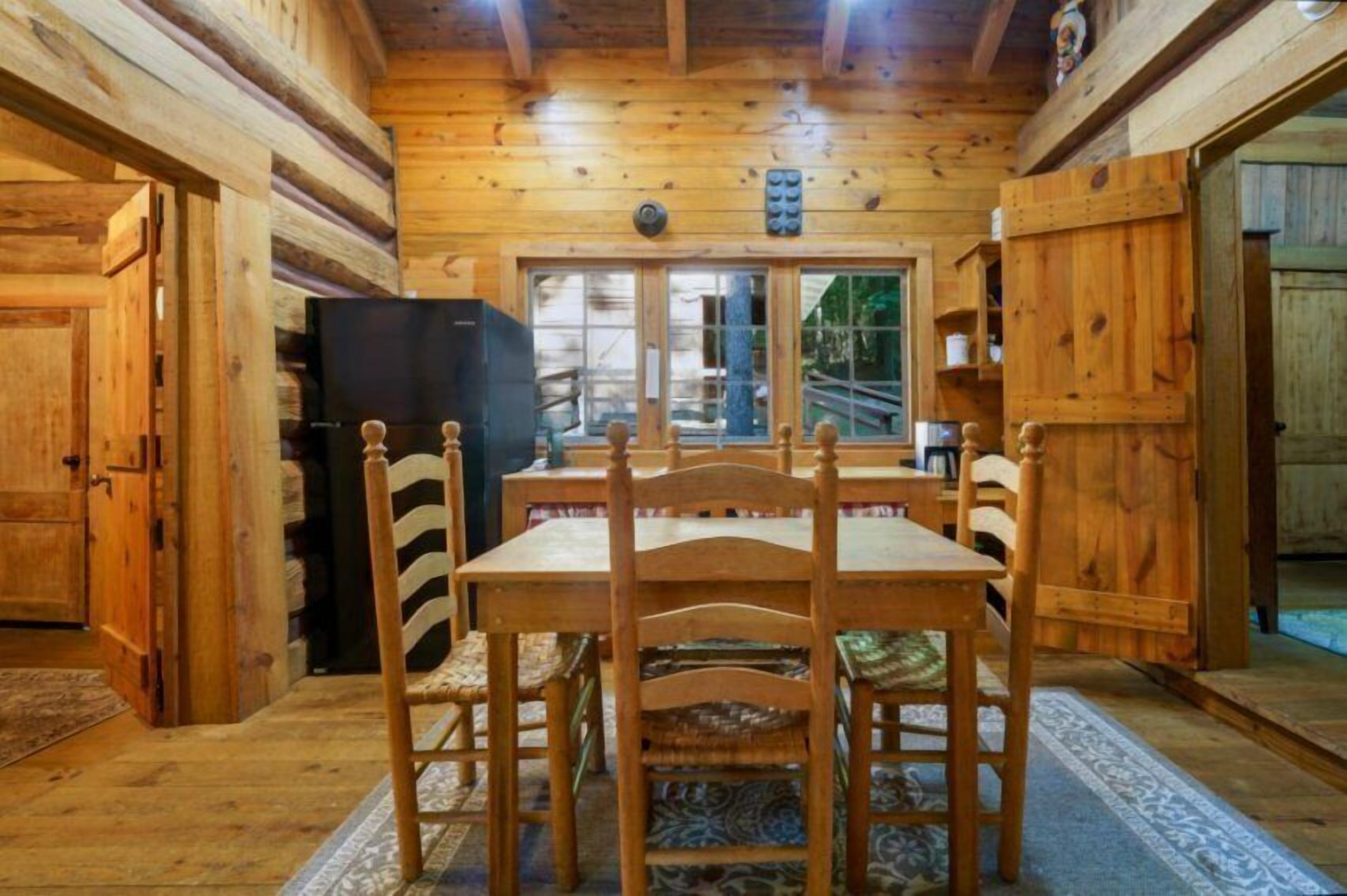 Een houten interieur met een eettafel en stoelen, een zwarte koelkast en een raam met uitzicht.