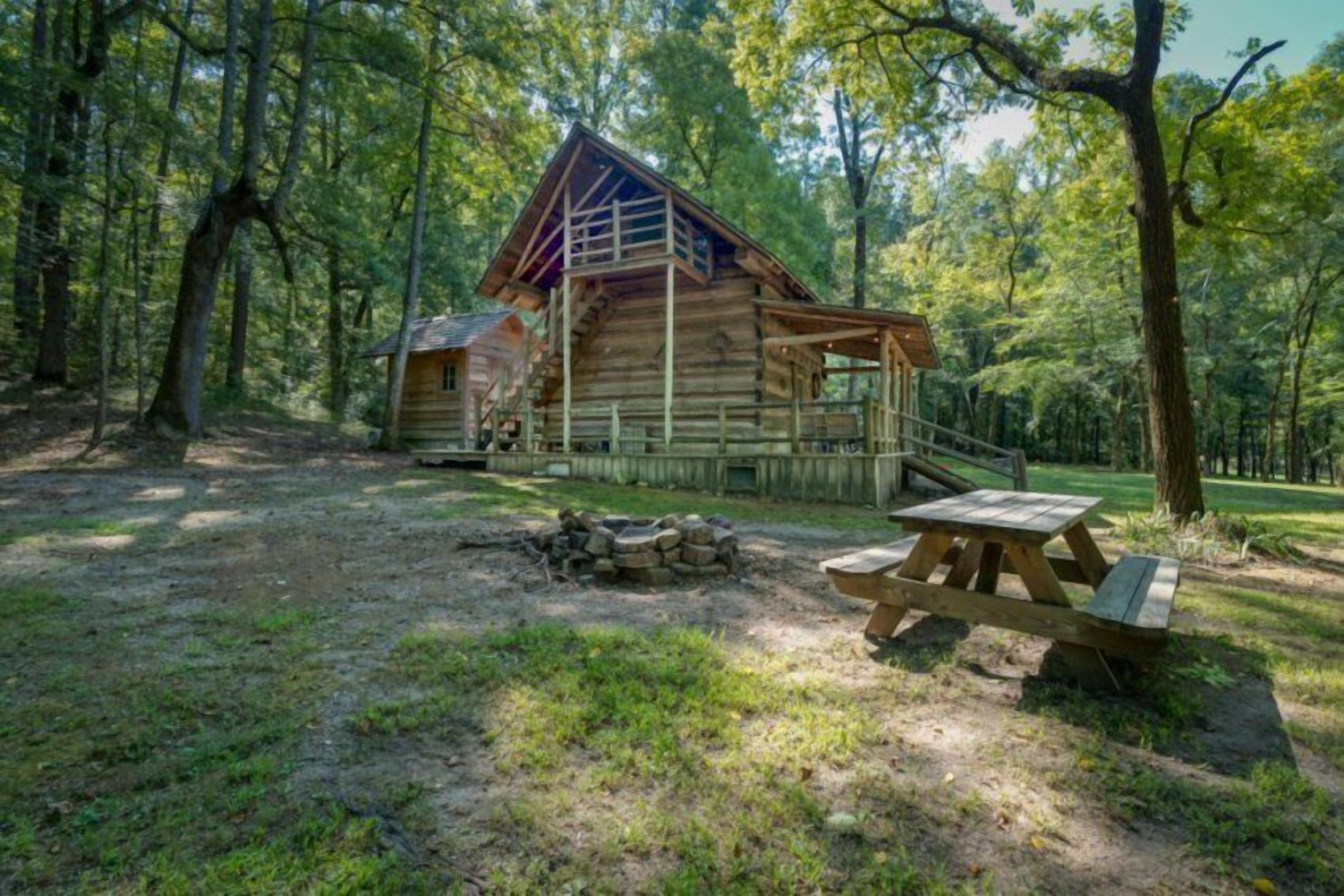 Een rustieke blokhut met een veranda en een picknicktafel in een bebost gebied.