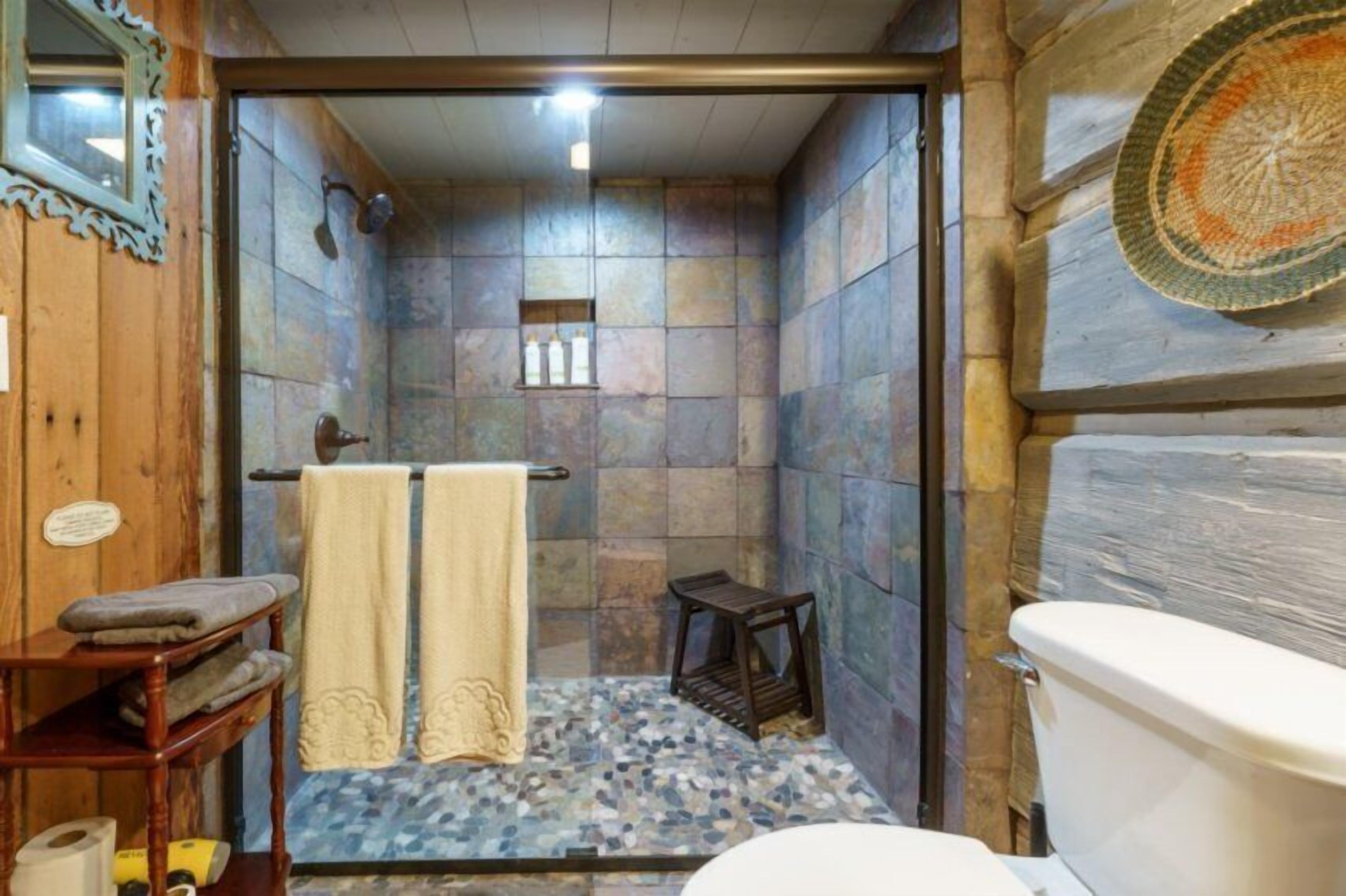 Een badkamer met een stenen muur, een houten bankje, een handdoekhouder en een toilet.