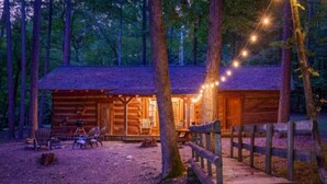 A rustic cabin with a wooden deck, outdoor seating, and string lights.