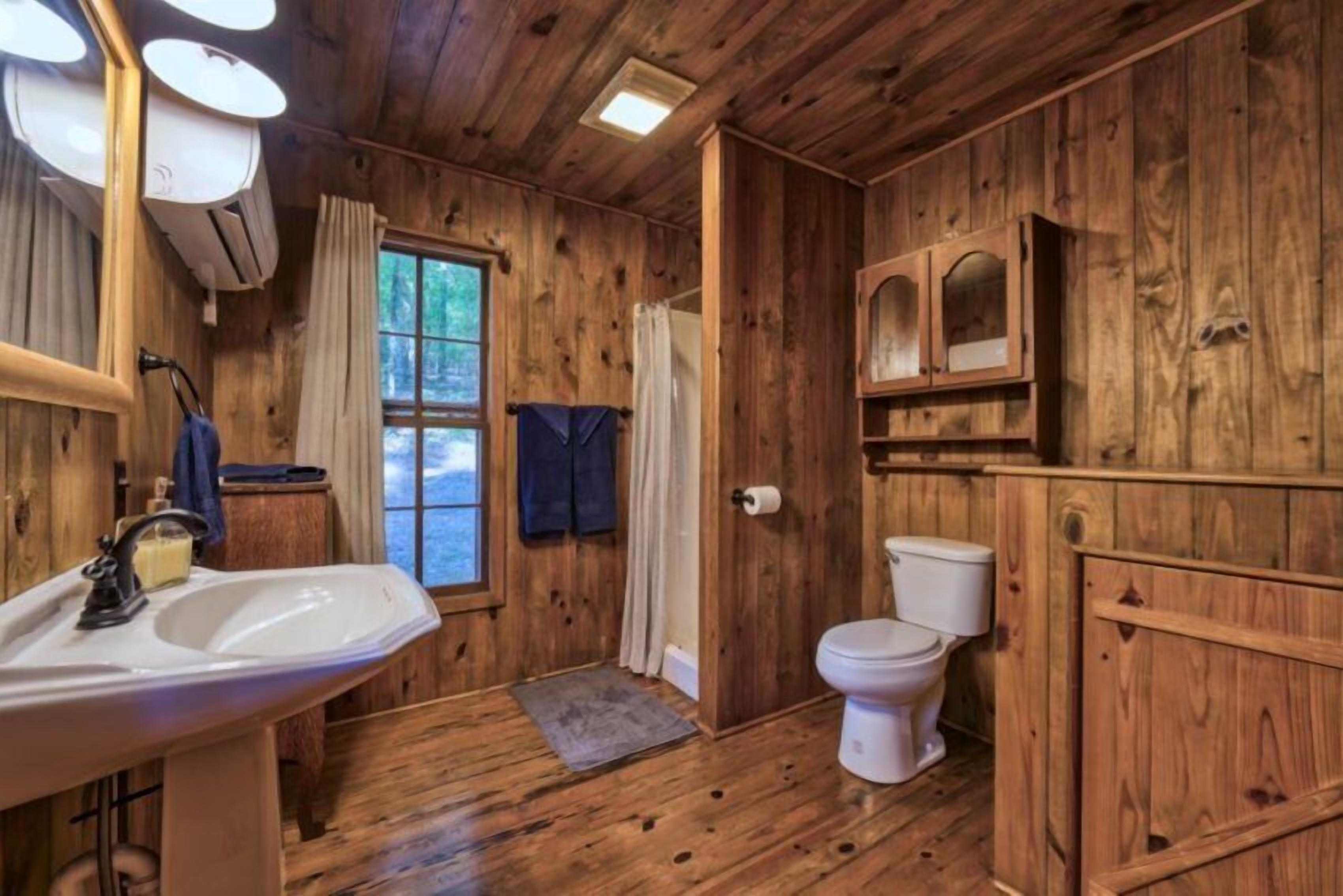 Ein Badezimmer einer Holzhütte mit Waschbecken, Toilette und einem Fenster mit Vorhängen.