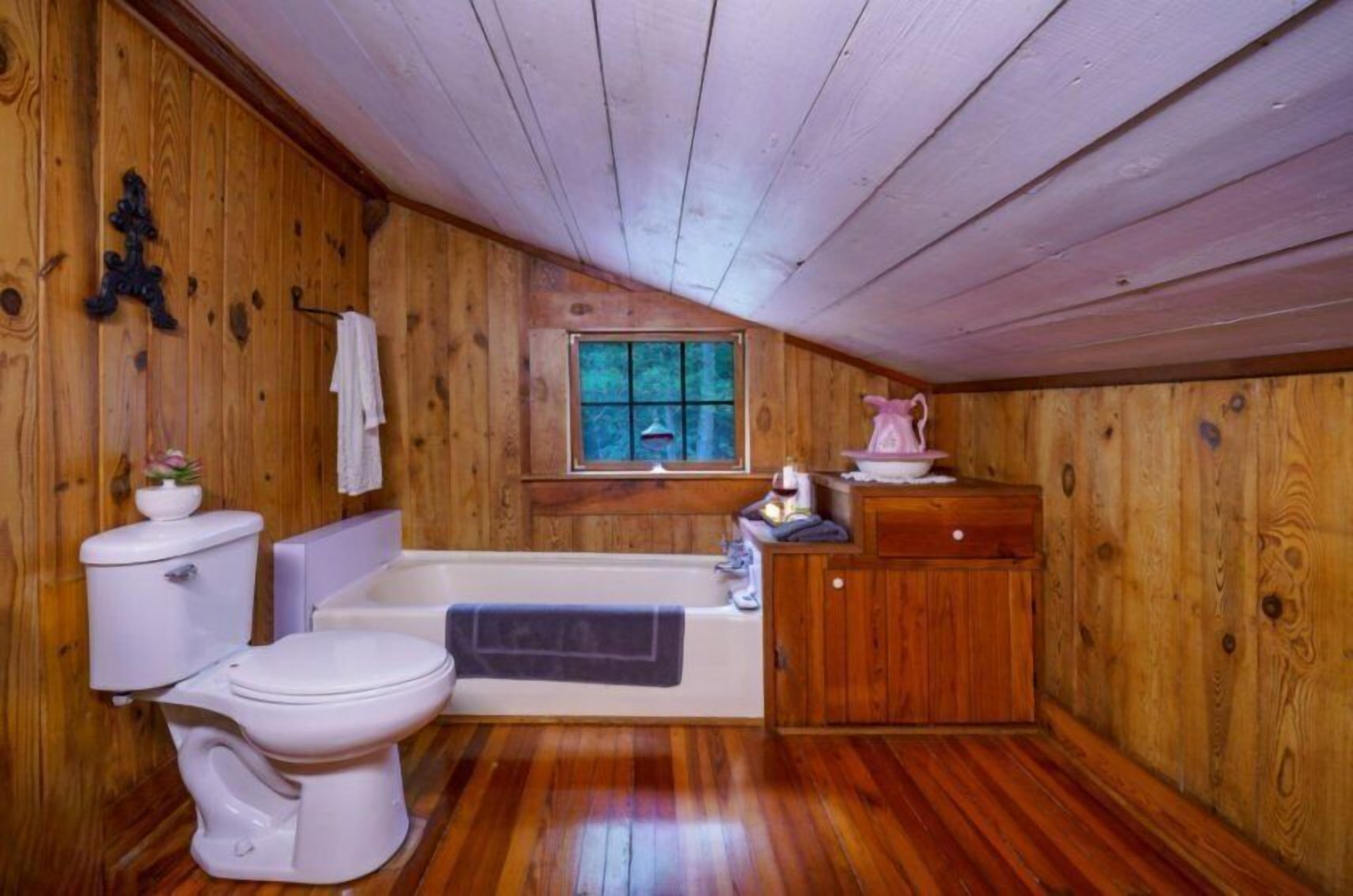A wooden-paneled bathroom with a toilet, bathtub, and wooden cabinet.