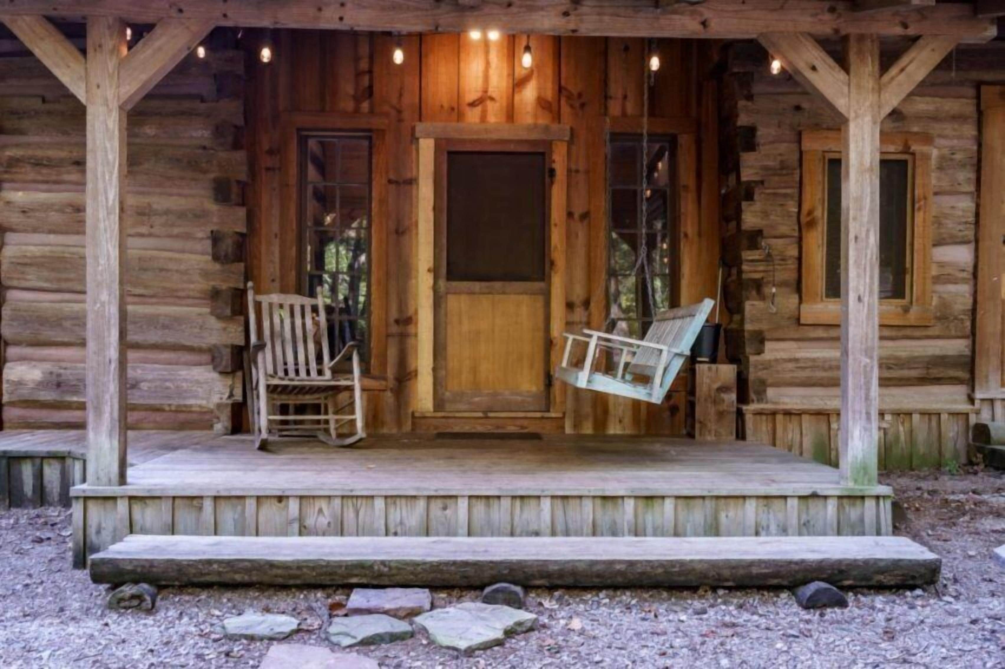 Une cabane en bois avec une véranda, deux fauteuils à bascule et une porte.
