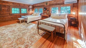A cabin with two beds, a wooden floor, and a large window.