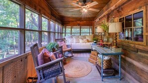 A cozy cabin interior with a rocking chair, a bed, and a table with books and a lamp.