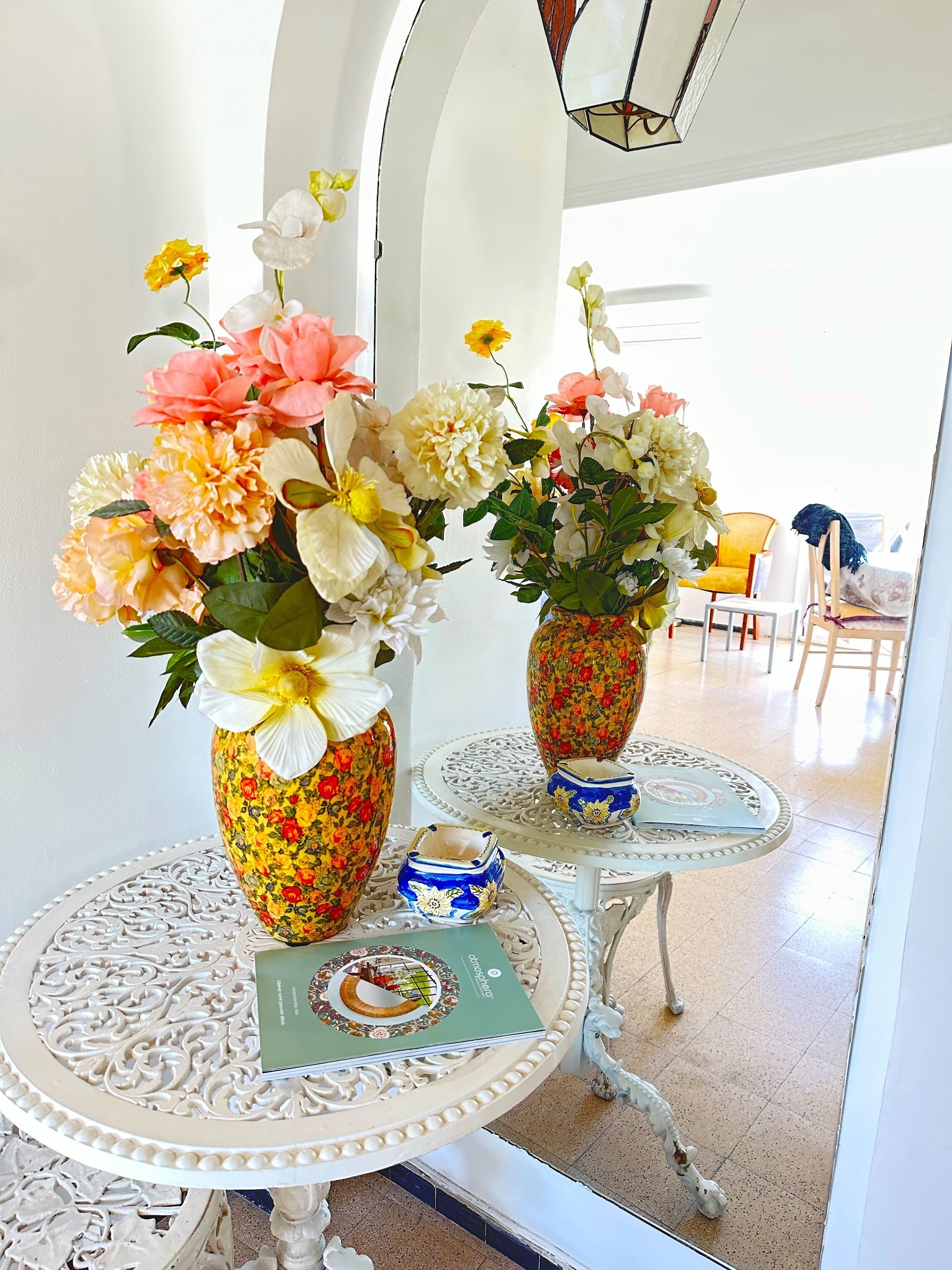 Two ornate vases with floral arrangements on a white table with intricate designs.