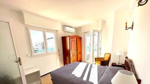 A hotel room with a bed, a chair, a desk, a lamp, and a wardrobe. - Viva Riviera Large 1 Bedroom with Sunny Terrace (Cannes)