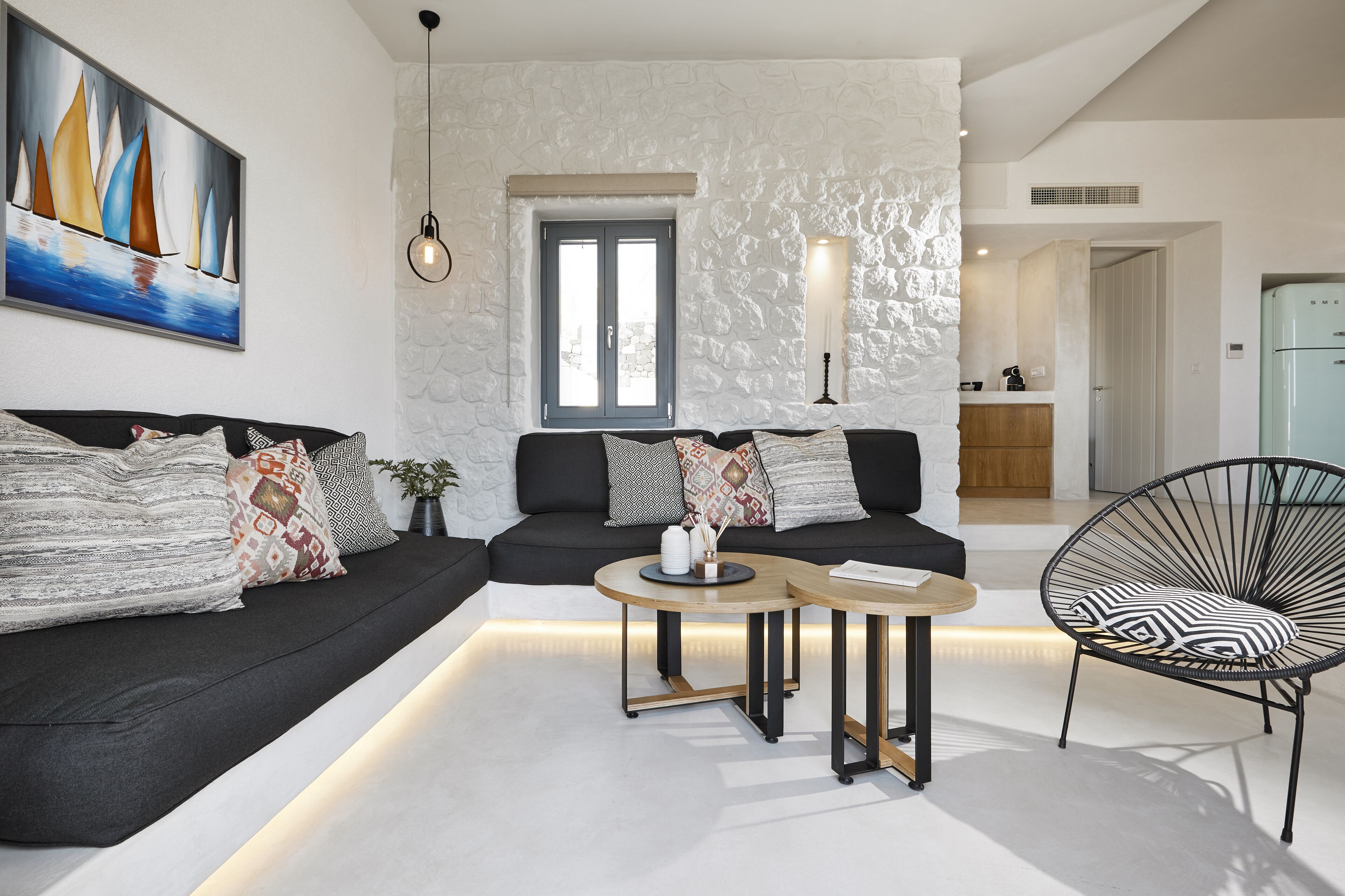 A modern living room with a black sofa, two round tables, a black chair, and a large painting of sailboats.