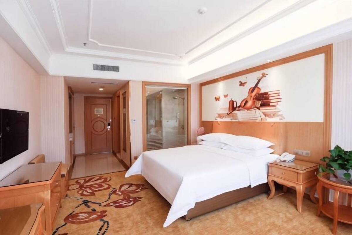 A hotel room with a bed, bedside table, TV, and a mirror.