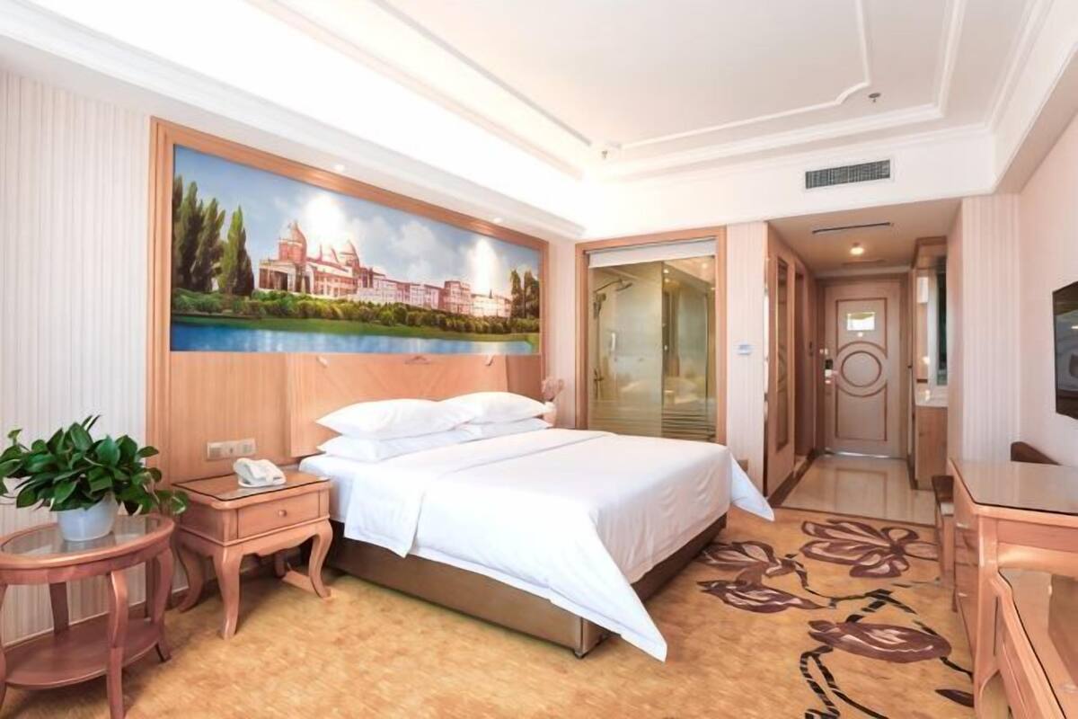 Une chambre d’hôtel avec un lit, une table de chevet, un téléphone, un tableau, une moquette et un téléviseur.