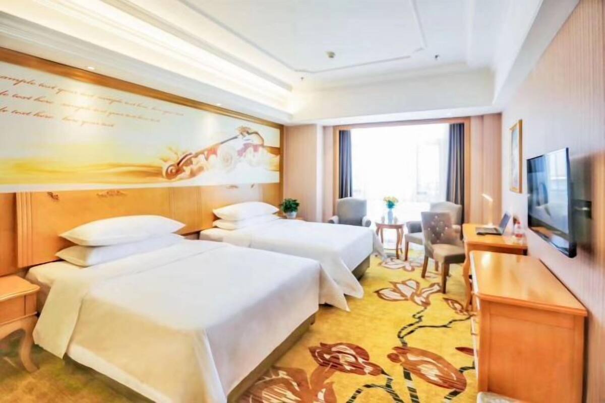 Une chambre d’hôtel avec deux lits, une télévision, un bureau, une chaise et une fenêtre.