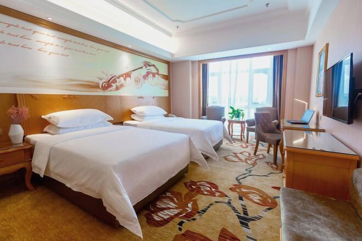 Une chambre d’hôtel avec deux lits, un bureau, une chaise, une télévision et une grande fenêtre.